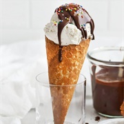 Vanilla Ice Cream Cone With Milk Chocolate Syrup, and Rainbow Spherical Sprinkles